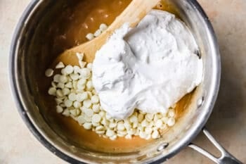 white chocolate chips and marshmallow creme stirred into caramelized sugar mixture in a saucepan with a wooden spoon.