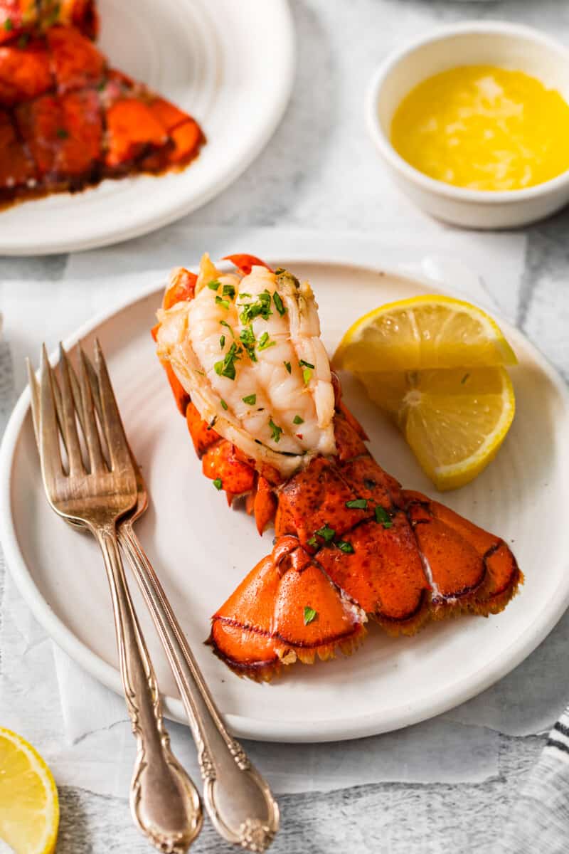 a lobster tail on a white plate with a fork and knife.