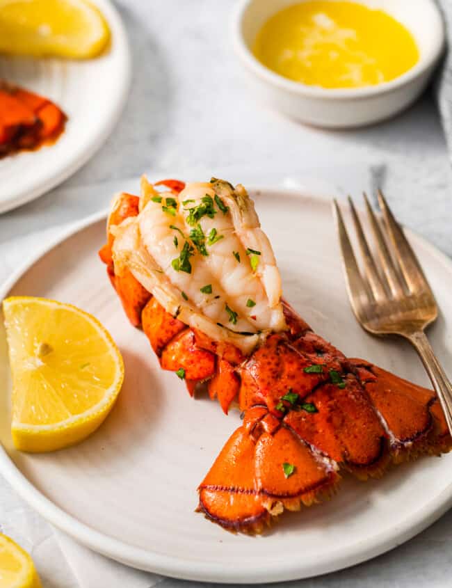a lobster tail on a white plate with a fork and knife.