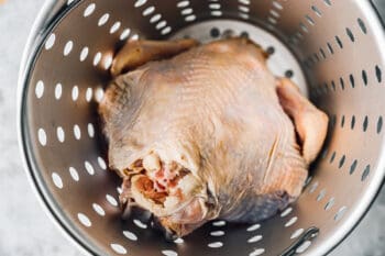 raw whole turkey in a strainer basket.