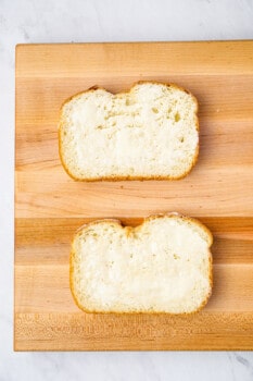 2 slices of buttered bread on a wooden cutting board.