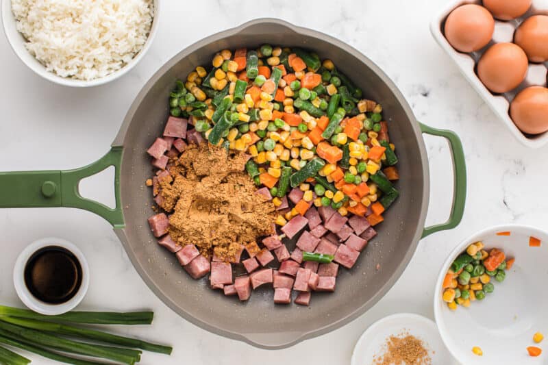 frozen vegetables, cubed ham, and fried rice seasoning in a frying pan.