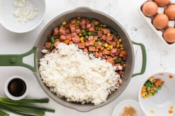 cooked rice added to sauteed vegetables and ham in a frying pan.