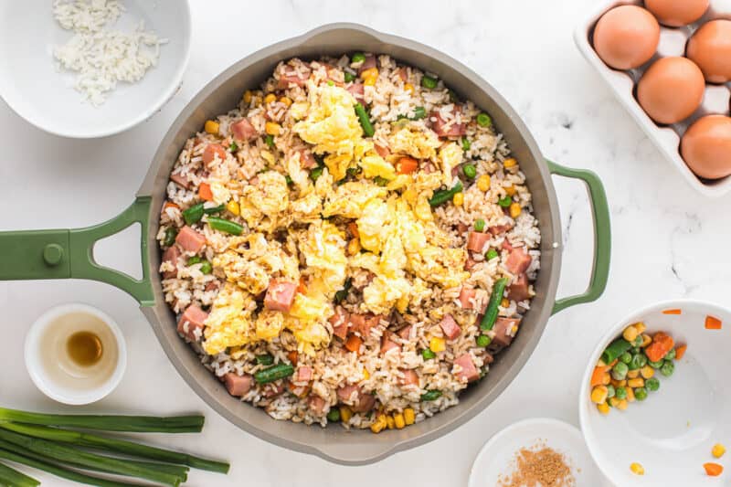 cooked egg added to ham fried rice in a frying pan.