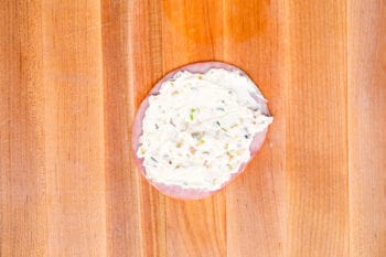 cream cheese spread on a slice of ham on a wooden cutting board.