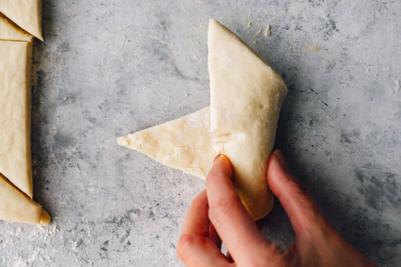 a hand rolling a triangle of croissant dough into a crescent shape.