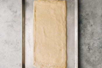 croissant dough rolled out into a long skinny rectangle on a baking sheet.