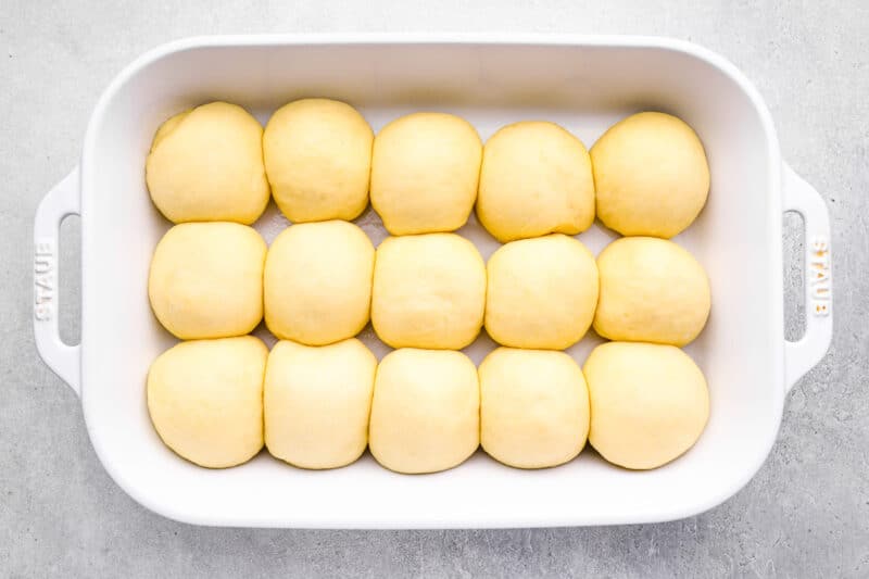15 proofed unbaked dinner rolls in a white baking dish.