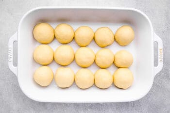 15 unbaked dinner rolls in a white baking pan.