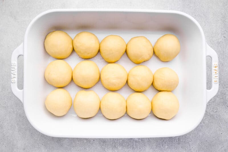 15 unbaked dinner rolls in a white baking pan.