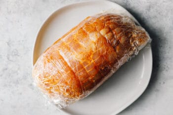 rubbed turkey breast wrapped in plastic wrap on a white plate.