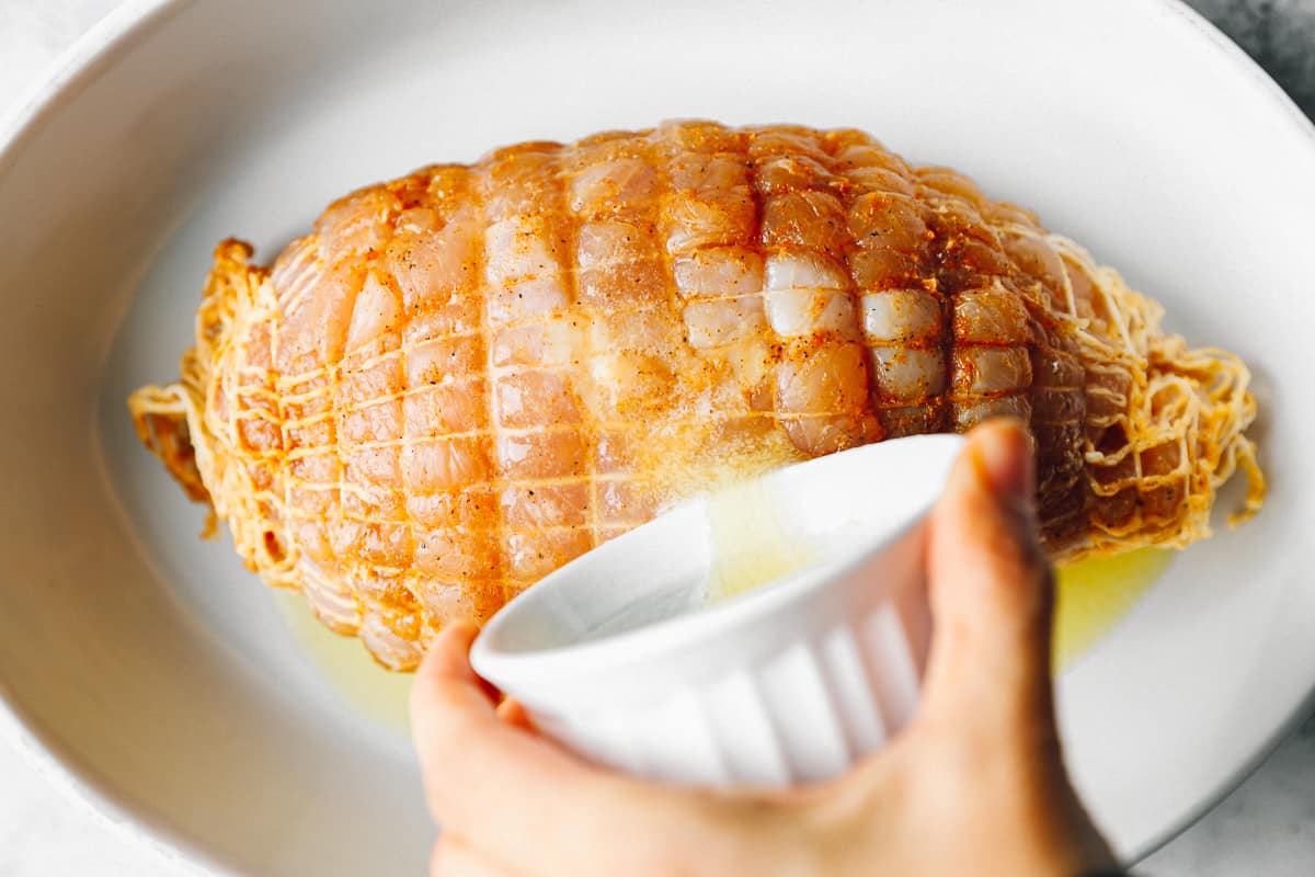 butter poured over honey baked turkey in a white baking dish.