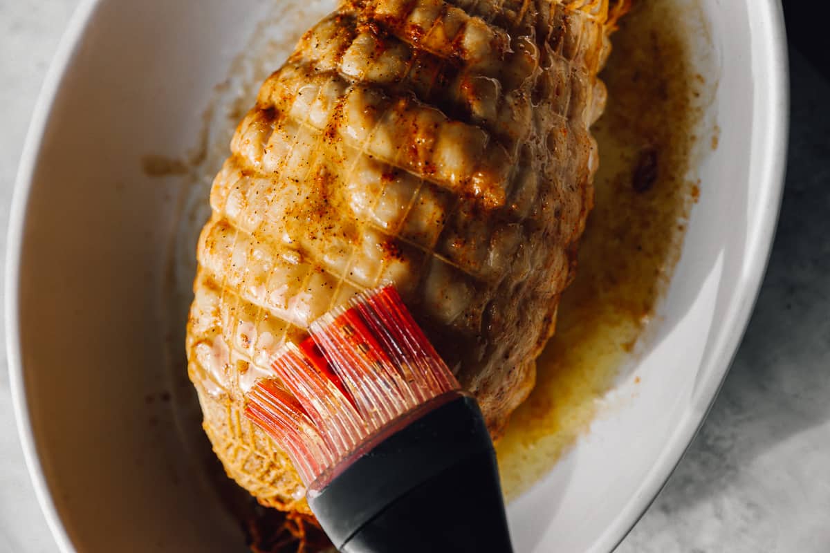 a basting brush brushing glaze over honey baked turkey breast in a baking dish.