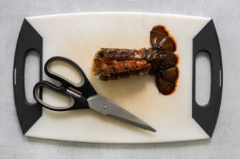 a cut lobster tail on a white cutting board with kitchen shears.