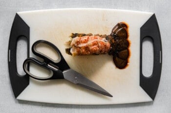 lobster meat removed from the tail on a white cutting board with kitchen shears.