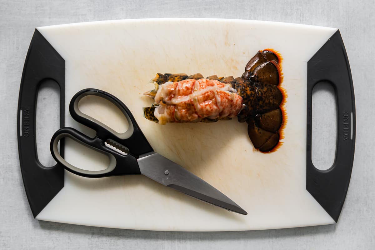 Lobster meat removed from the tail on a white cutting board with kitchen shears. - 7