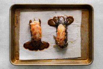 two prepared lobster tails on a baking sheet.