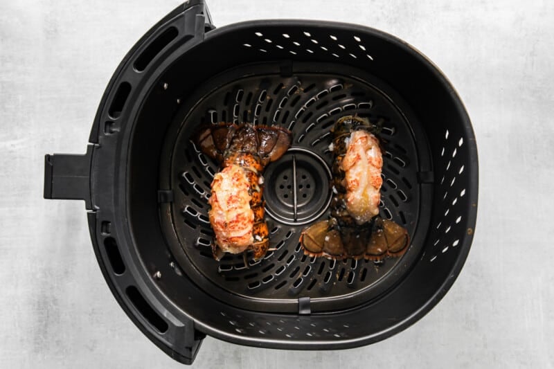two prepared lobster tails in the basket of an air fryer.