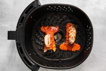 two cooked lobster tails in the basket of an air fryer.