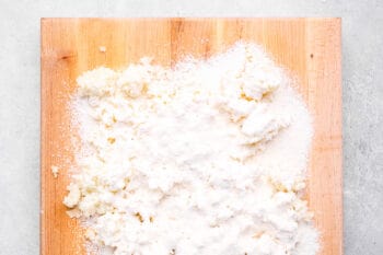 flour poured over mashed potato mixture on a wooden cutting board.