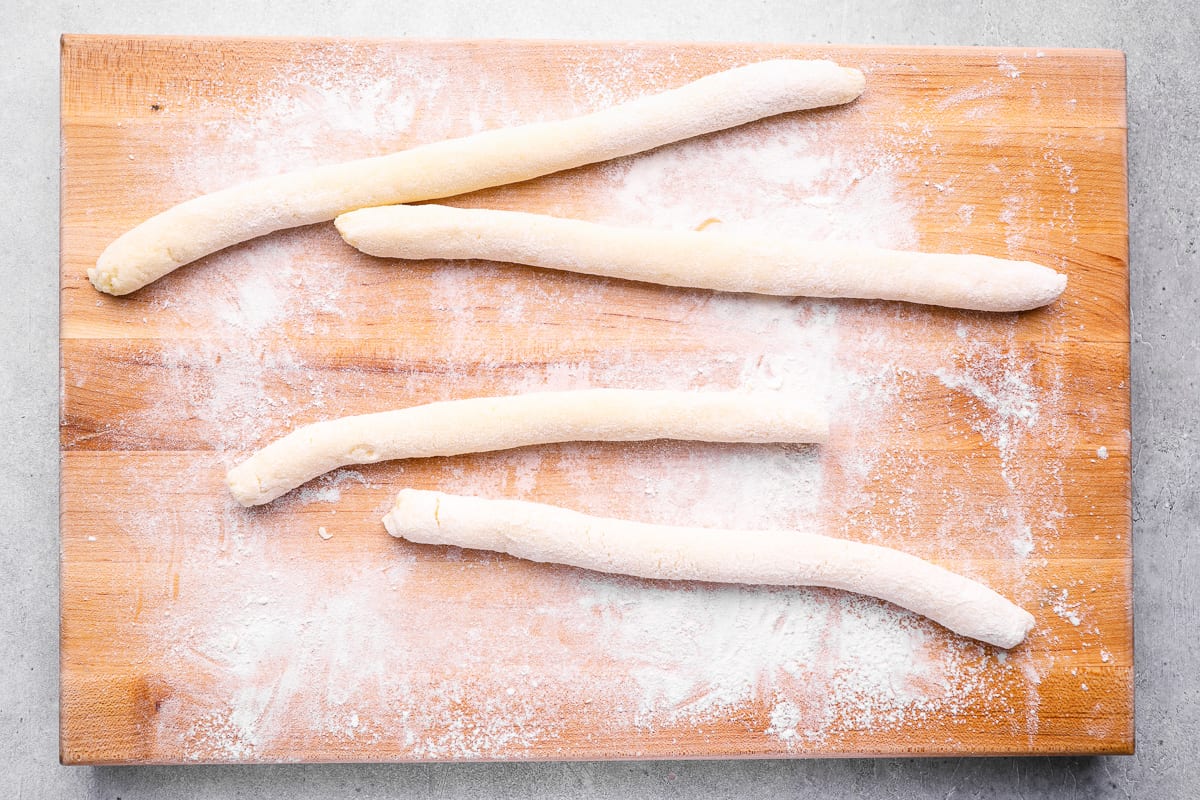 4 gnocchi dough ropes on a floured wooden cutting board.