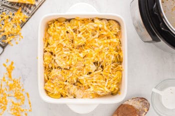 cheese sprinkled over instant pot scalloped potatoes in a white square baking dish.