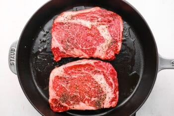 2 seasoned ribeye steaks in a cast iron pan.