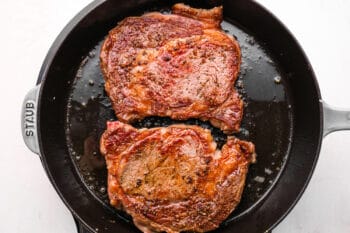 2 partially seared ribeye steaks in a cast iron pan.