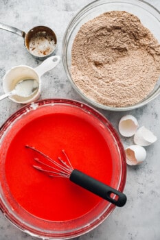 wet and dry ingredients for red velvet cake in glass bowls with a whisk.