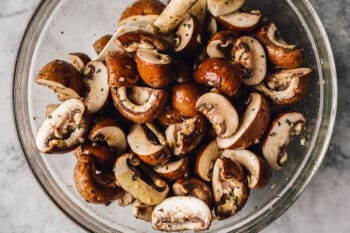 mushrooms tossed with seasoning in a glass bowl.