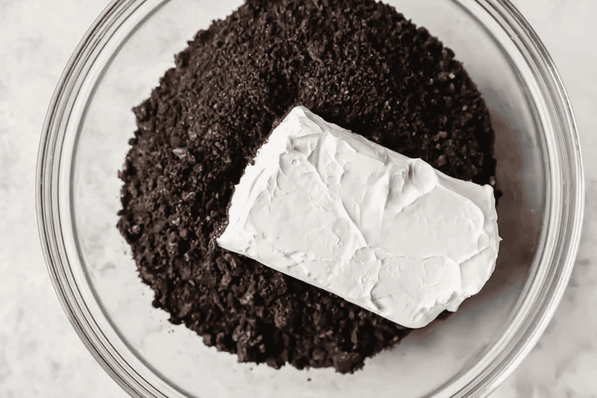 Oreo crumbs and cream cheese in a glass bowl.