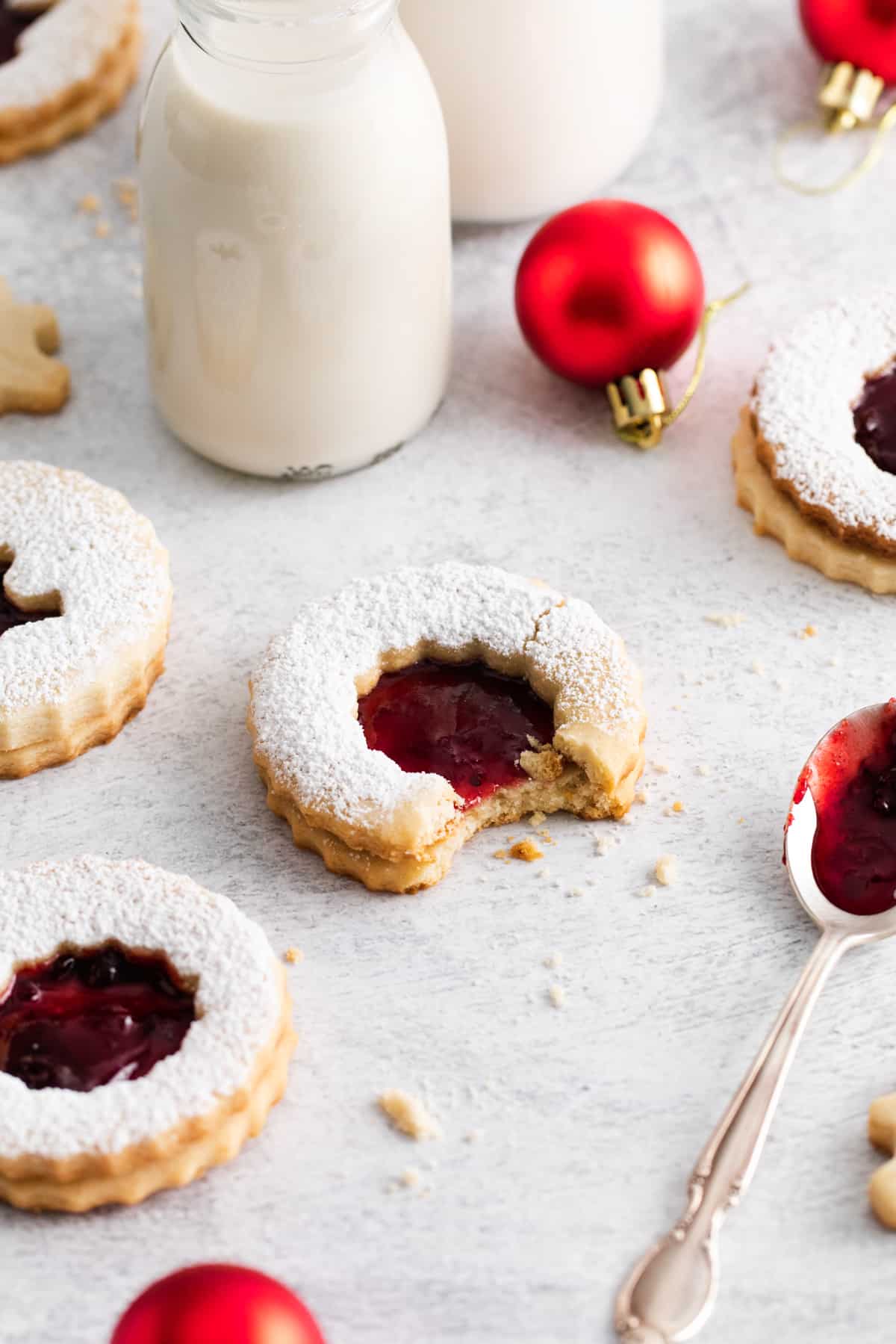 Linzer cookies arranged on a tablescape along with christmas ornaments and jars of milk