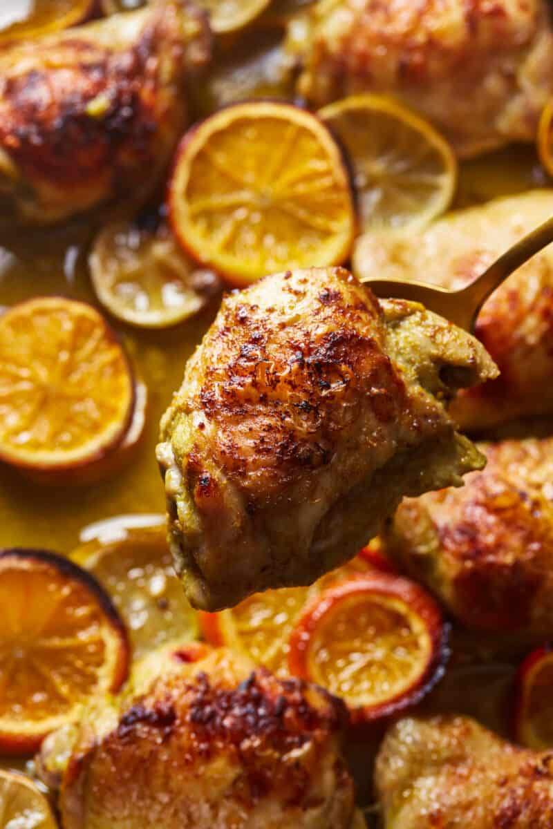 spatula holding up a baked chicken thigh, above a pan of chicken