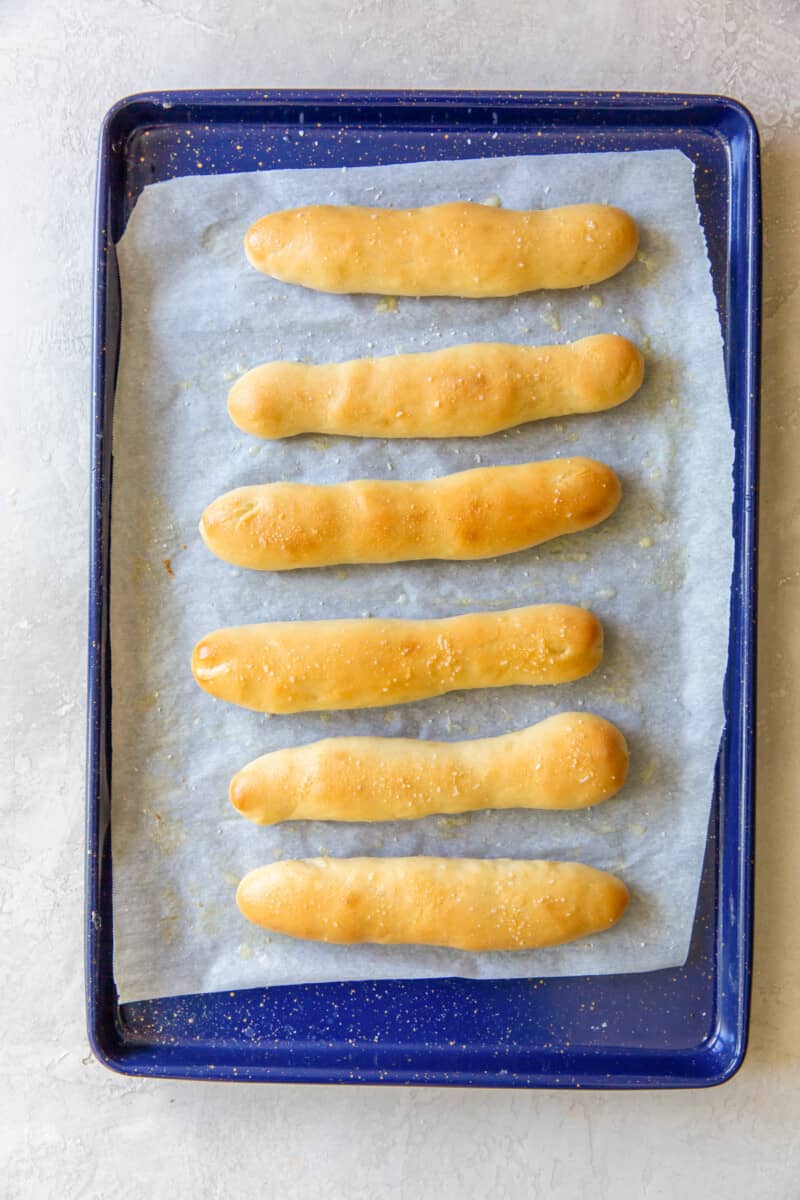 6 olive garden breadsticks on a blue baking sheet.