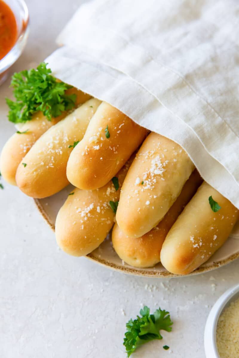 close up of olive garden breadsticks on a white plate with a towel draped over them.