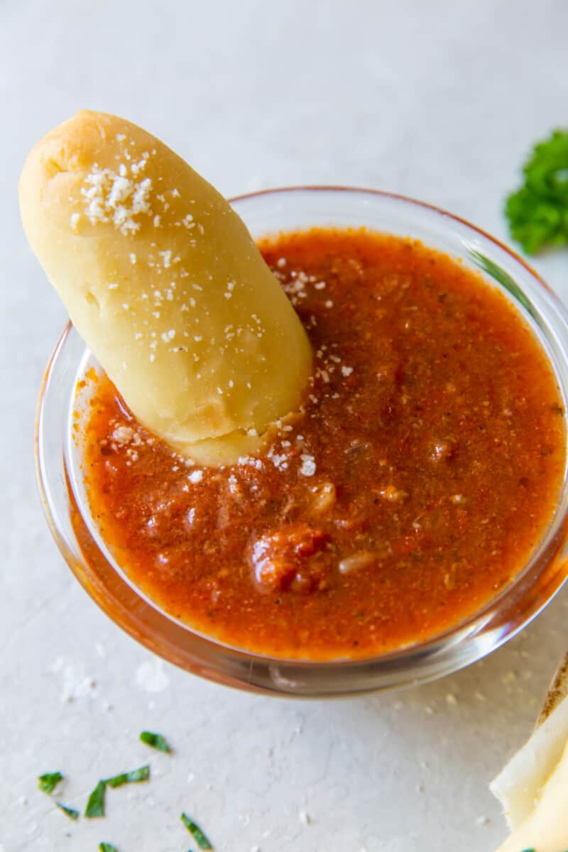 an olive garden breadstick being dipped into a bowl of marinara sauce.