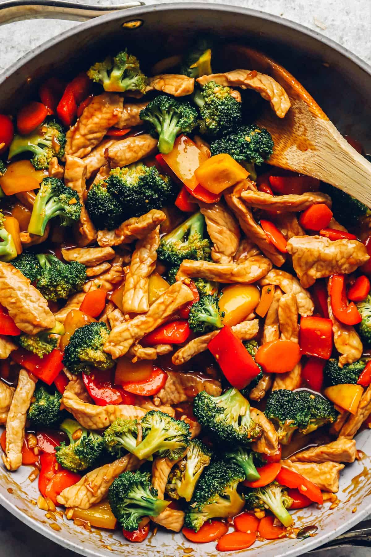 close up of stir fried pork and vegetables in a skillet with a wooden spoon.