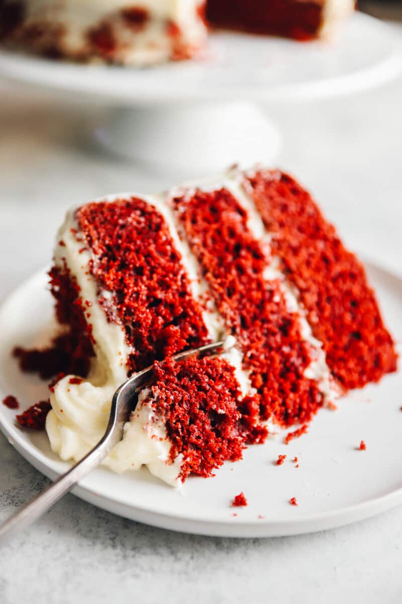 a fork cutting a slice of red velvet cake on a white plate.