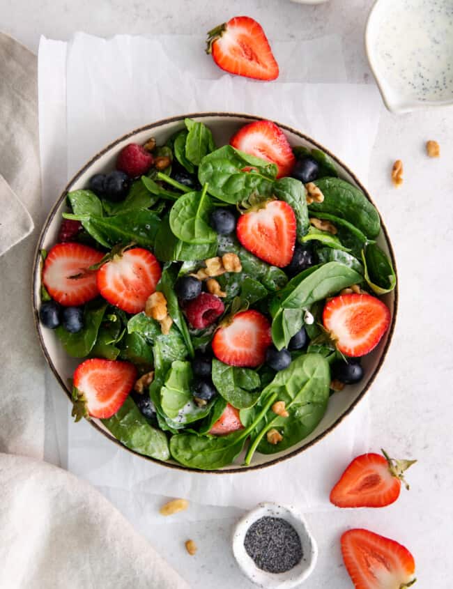 overhead view of spinach berry salad in a beige bowl.