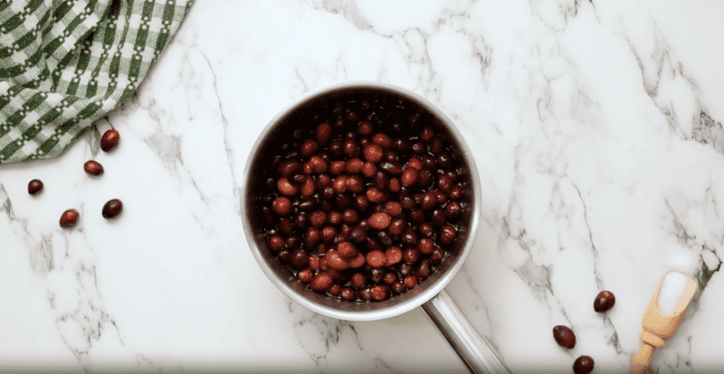 A pan filled with red beans topped with sugared cranberries on a marble countertop.