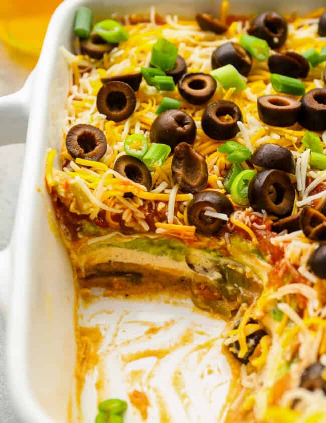 close up of partially eaten 7 layer dip in a rectangular baking pan.