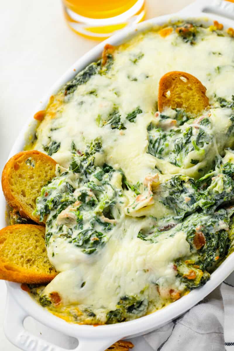 bacon spinach dip in an oval baking dish with toasted bread pieces stuck in.