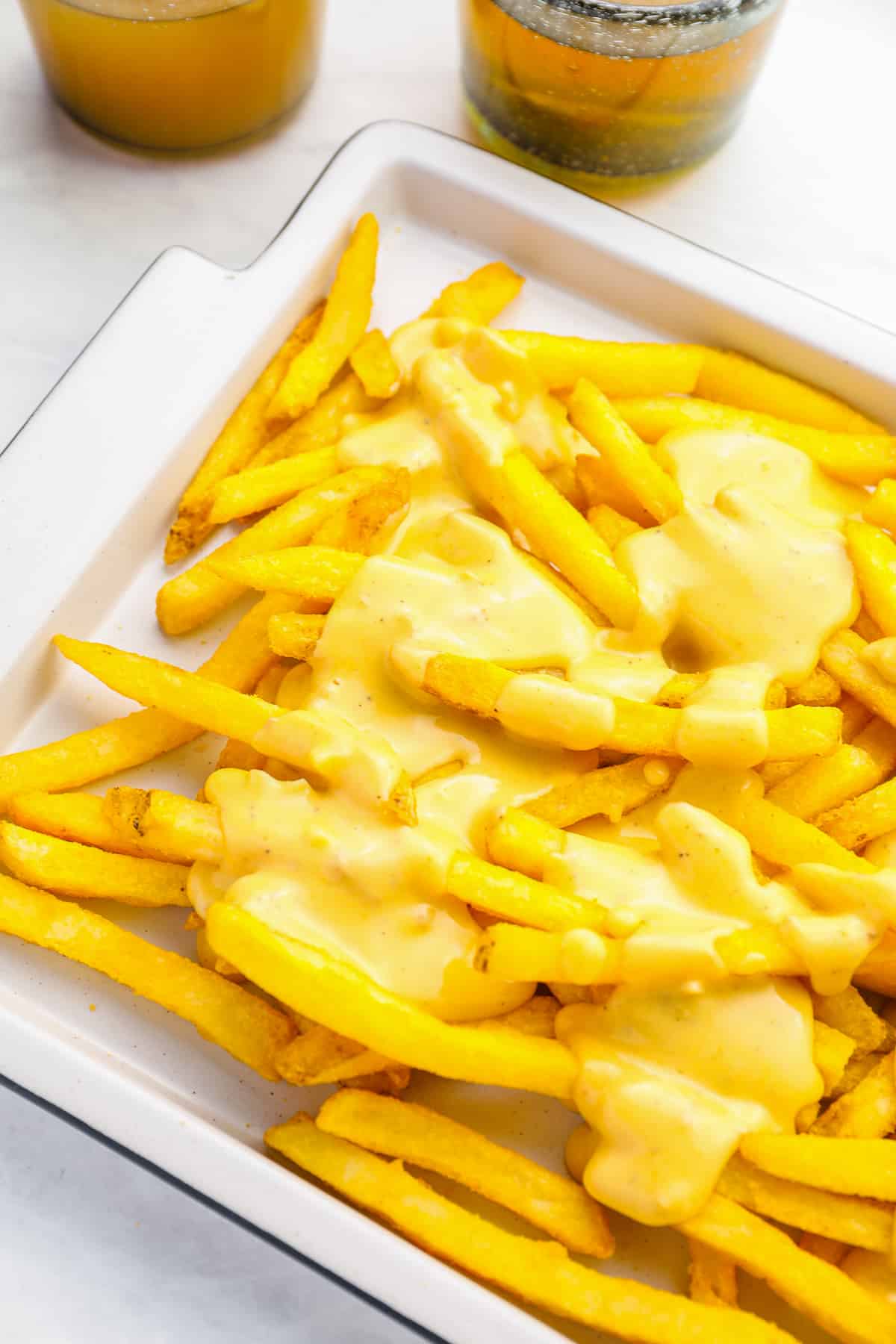 partial view of cheese fries on a white rectangular serving dish.