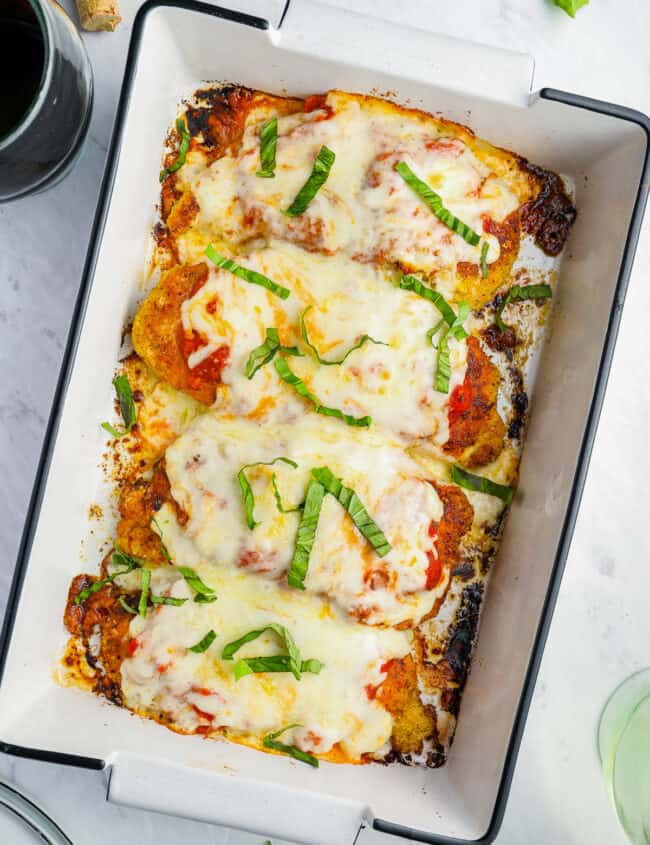 overhead view of chicken parmesan in a white rectangular baking pan topped with shredded basil.