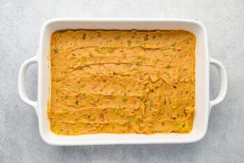 refried beans and chiles spread in the bottom of a rectangular baking pan.