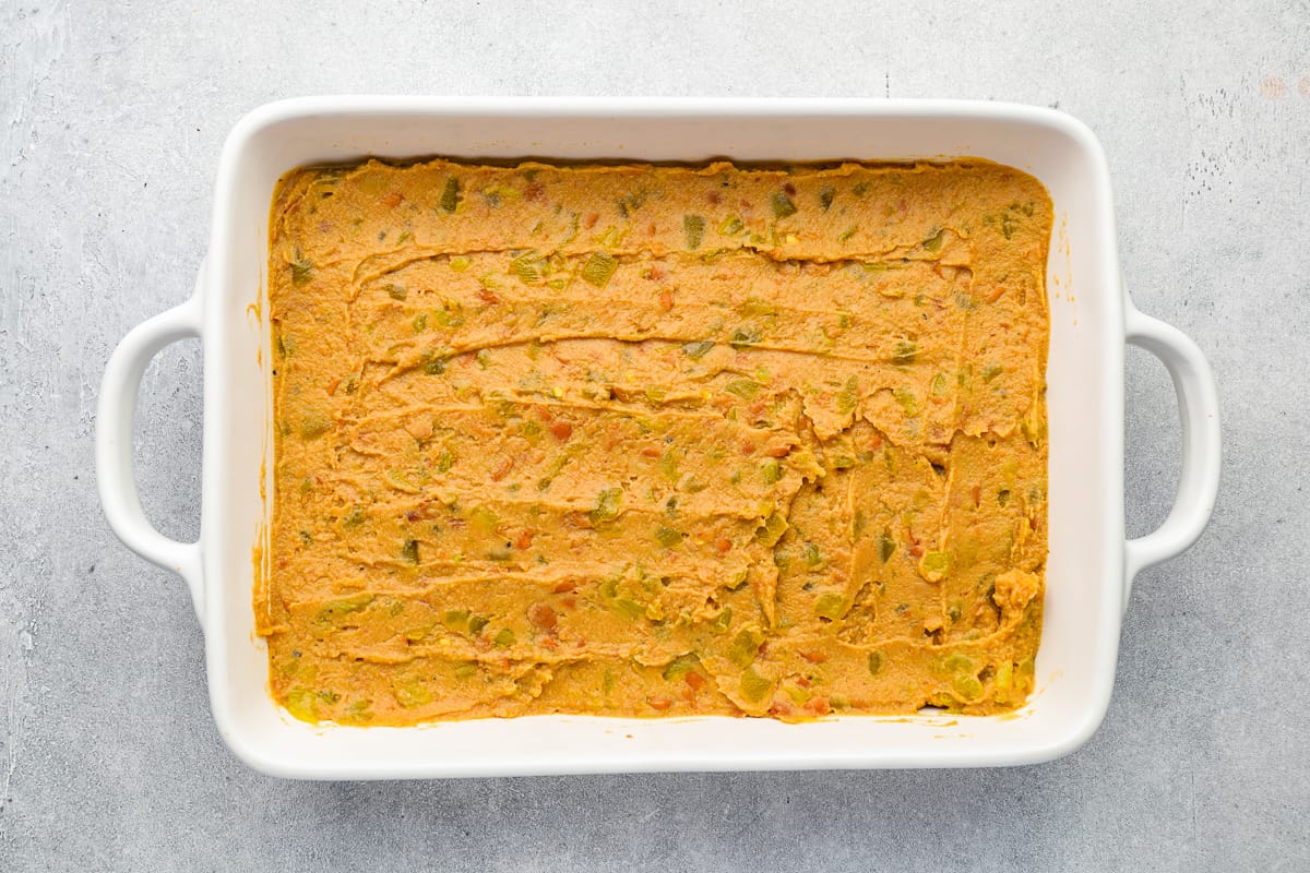 Refried beans and chiles spread in the bottom of a rectangular baking pan.