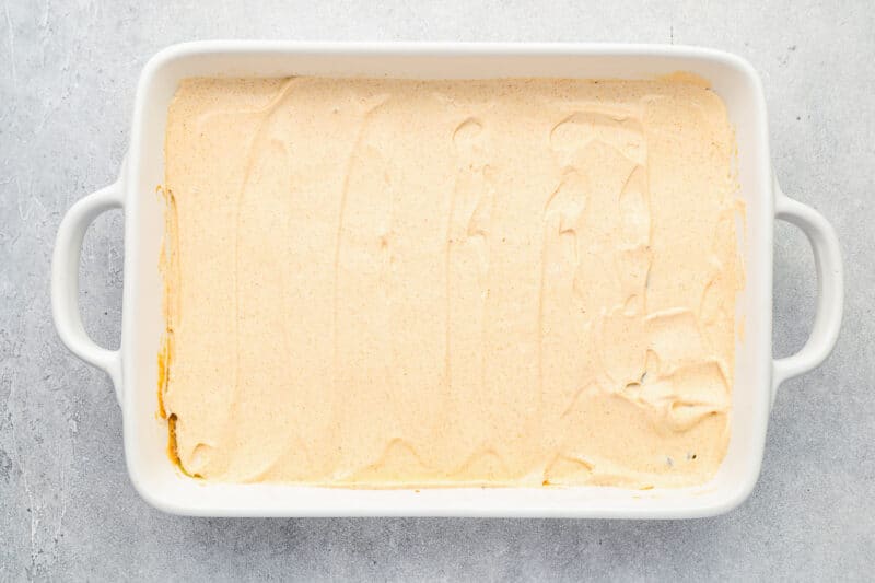 sour cream and taco seasoning spread over refried beans and chiles in a rectangular baking pan.