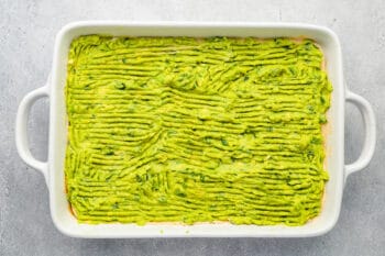 guacamole spread over sour cream layer in a rectangular baking dish.