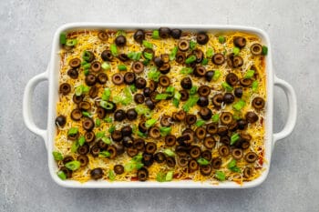 overhead view of 7 layer dip in a rectangular baking pan topped with black olives and green onions.