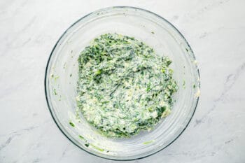 spinach and cheese added to cream cheese mixture in a glass bowl.